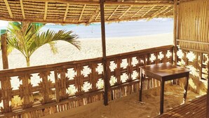 Uma cabana à beira-mar com telhado de palha, grade de madeira e uma mesa.