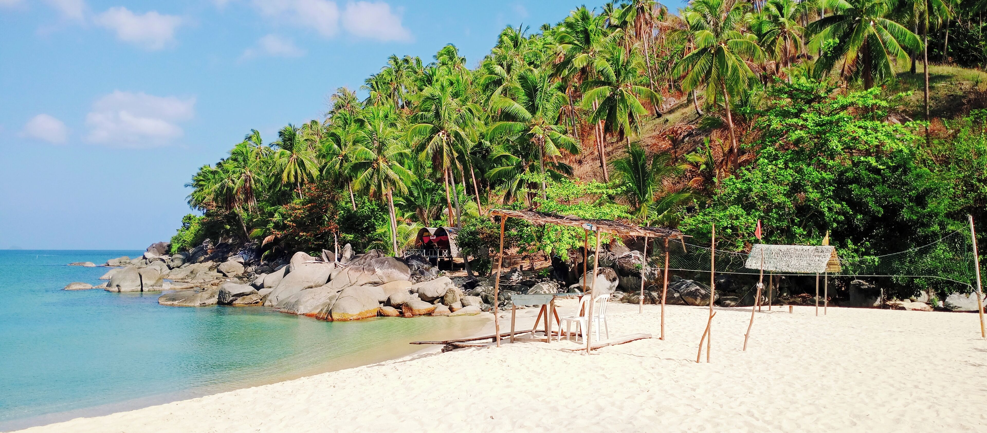 A beach with clear turquoise water, white sand, and a rocky outcrop with palm trees.