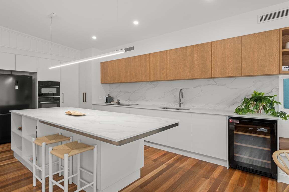 A modern kitchen with white cabinetry, a marble countertop, and wooden flooring.