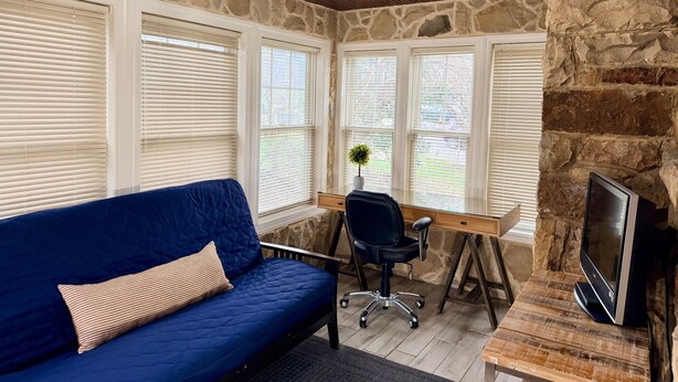 A room with a stone wall, a blue sofa, a desk with a chair, and a television.