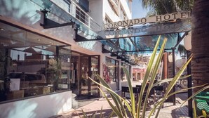 Exterior del Hotel Coronado, con fachada de vidrio, zona de estar al aire libre y palmeras.