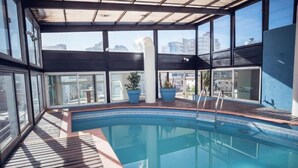 Una piscina en la azotea con vistas despejadas del horizonte de la ciudad, rodeada de grandes ventanales y plantas en macetas.