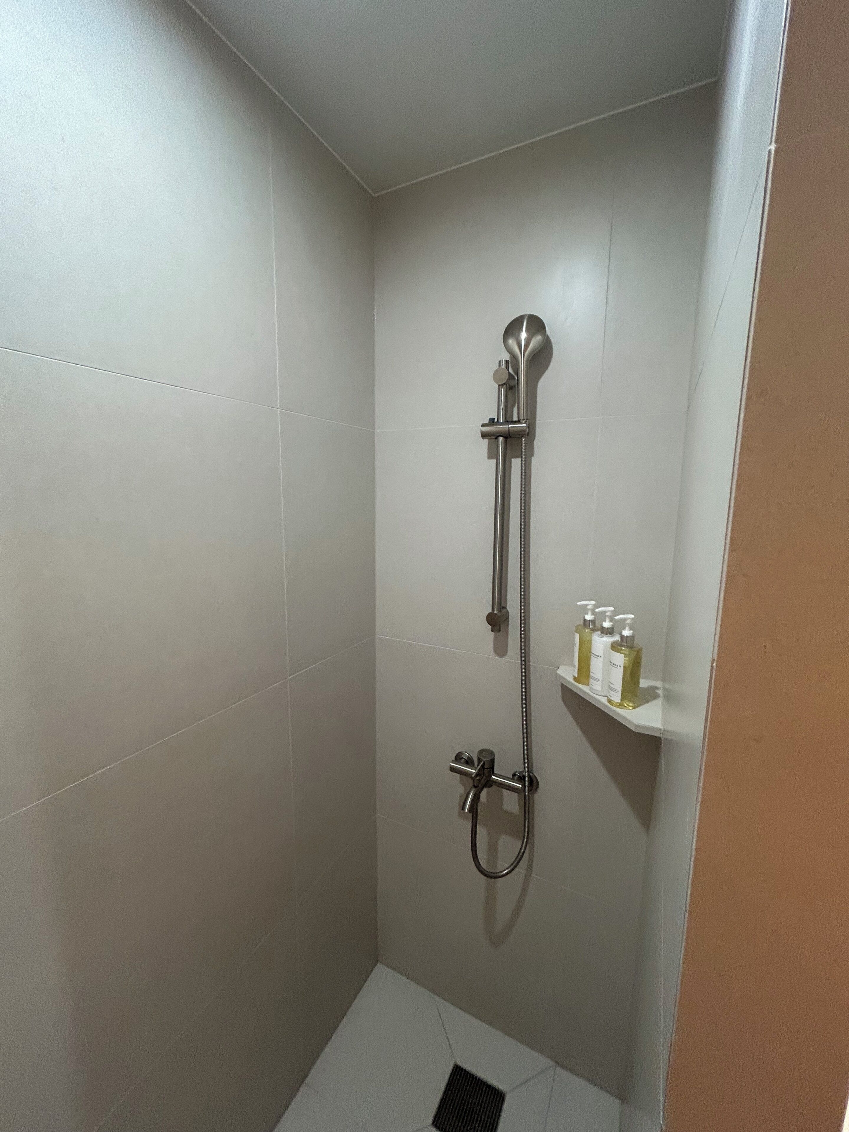 A small, tiled shower room with a handheld showerhead and a wall-mounted faucet.