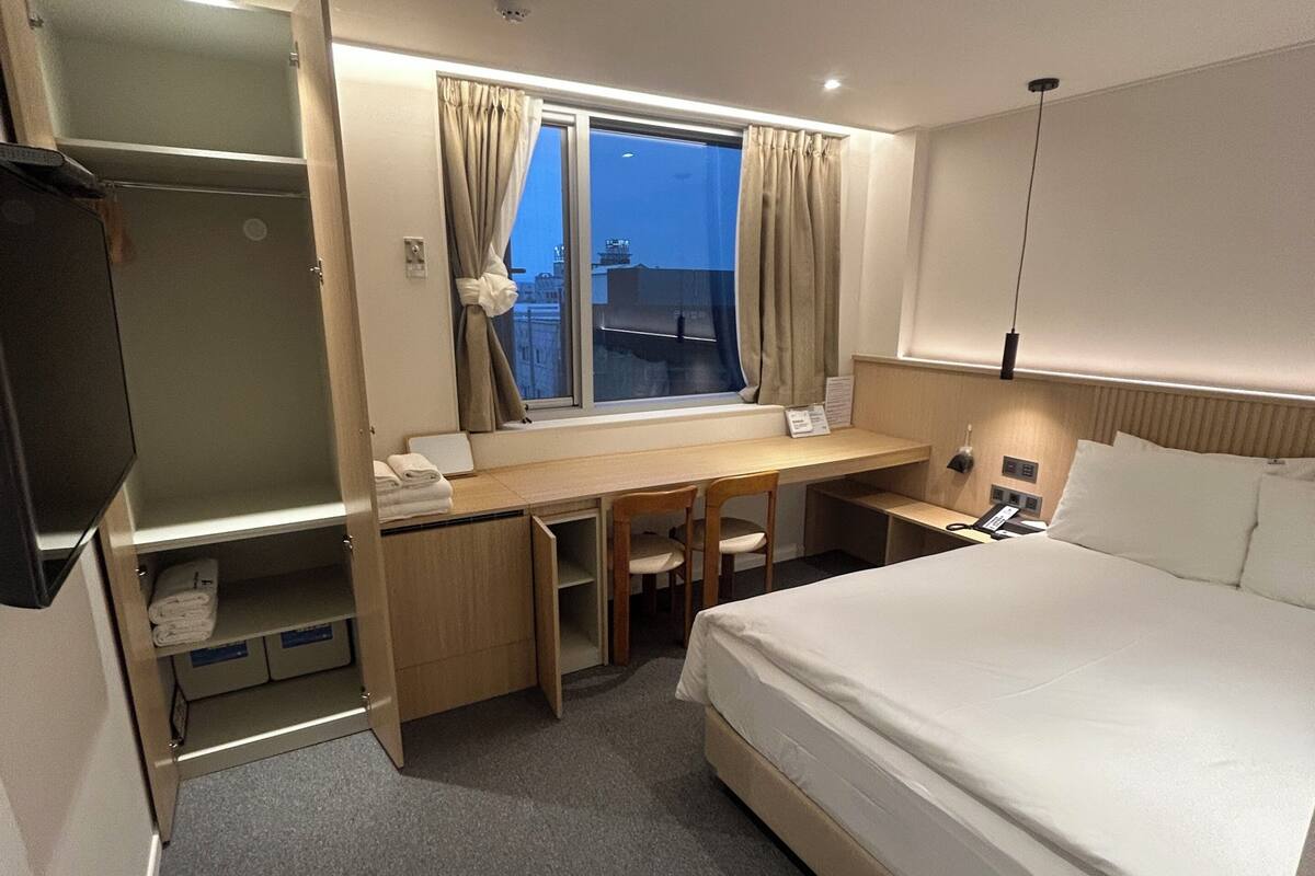 A hotel room with a bed, desk, chair, and a window with curtains.