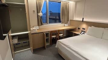A hotel room with a bed, desk, chair, and a window with curtains.