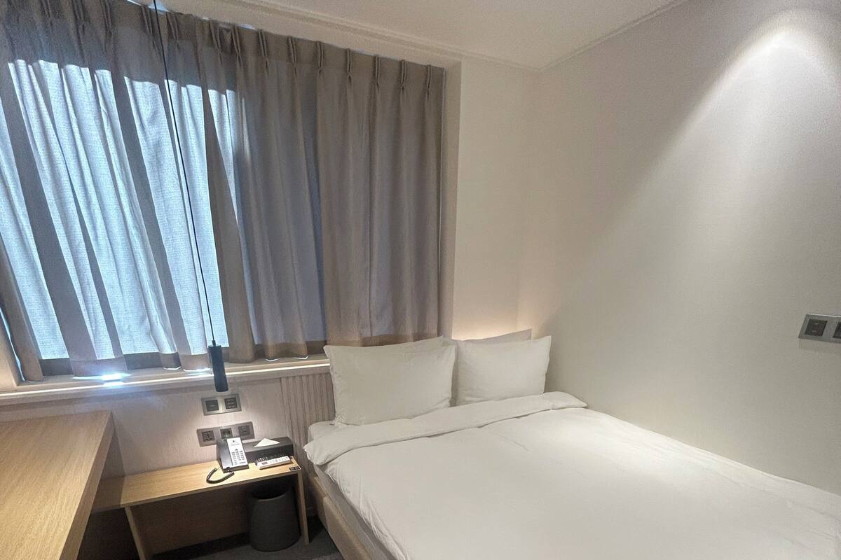 A hotel room with a bed, bedside tables, a desk, a lamp, and a window with curtains.
