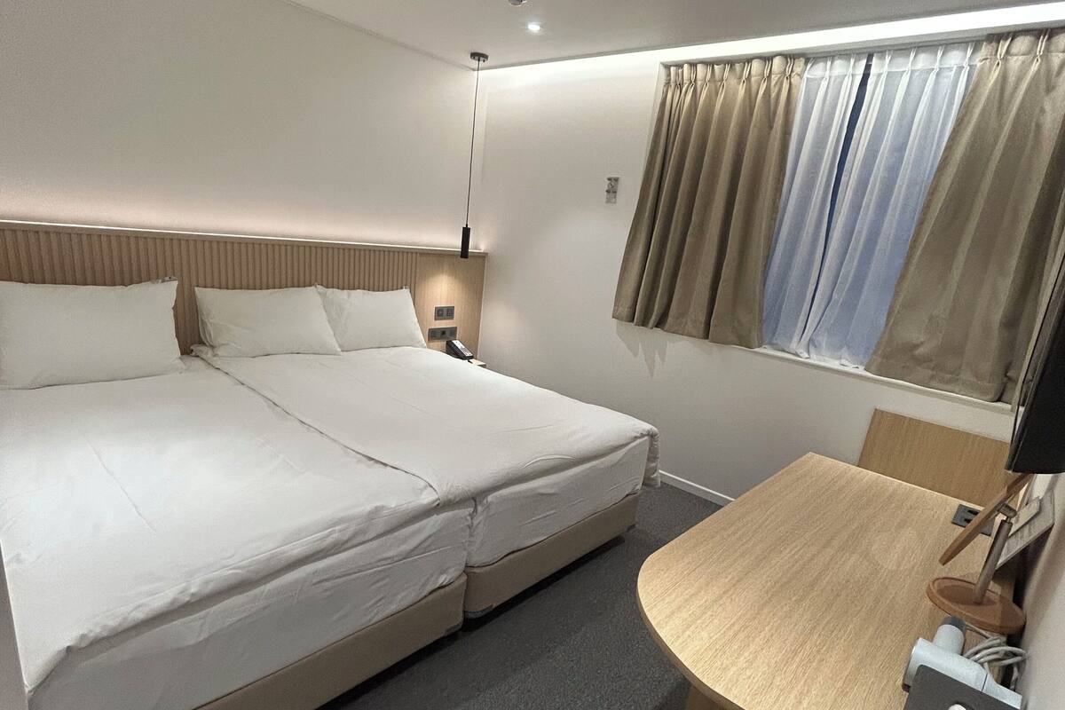 A hotel room with a bed, bedside table, lamp, and a small desk area.