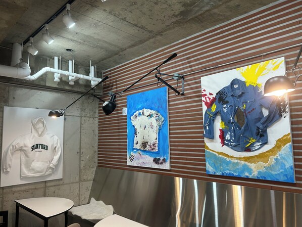 A room with a concrete ceiling, exposed pipes, a table, and a wall with striped pattern and artwork.