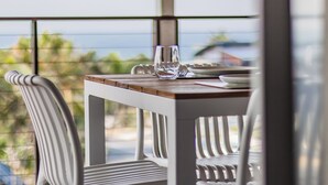 Une table à manger avec des chaises, un verre et des assiettes, le tout placé devant une vue sur l’océan.
