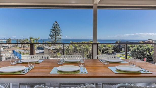 Un espace repas avec des tables préparées pour deux personnes, offrant une vue panoramique sur l’océan et les palmiers.