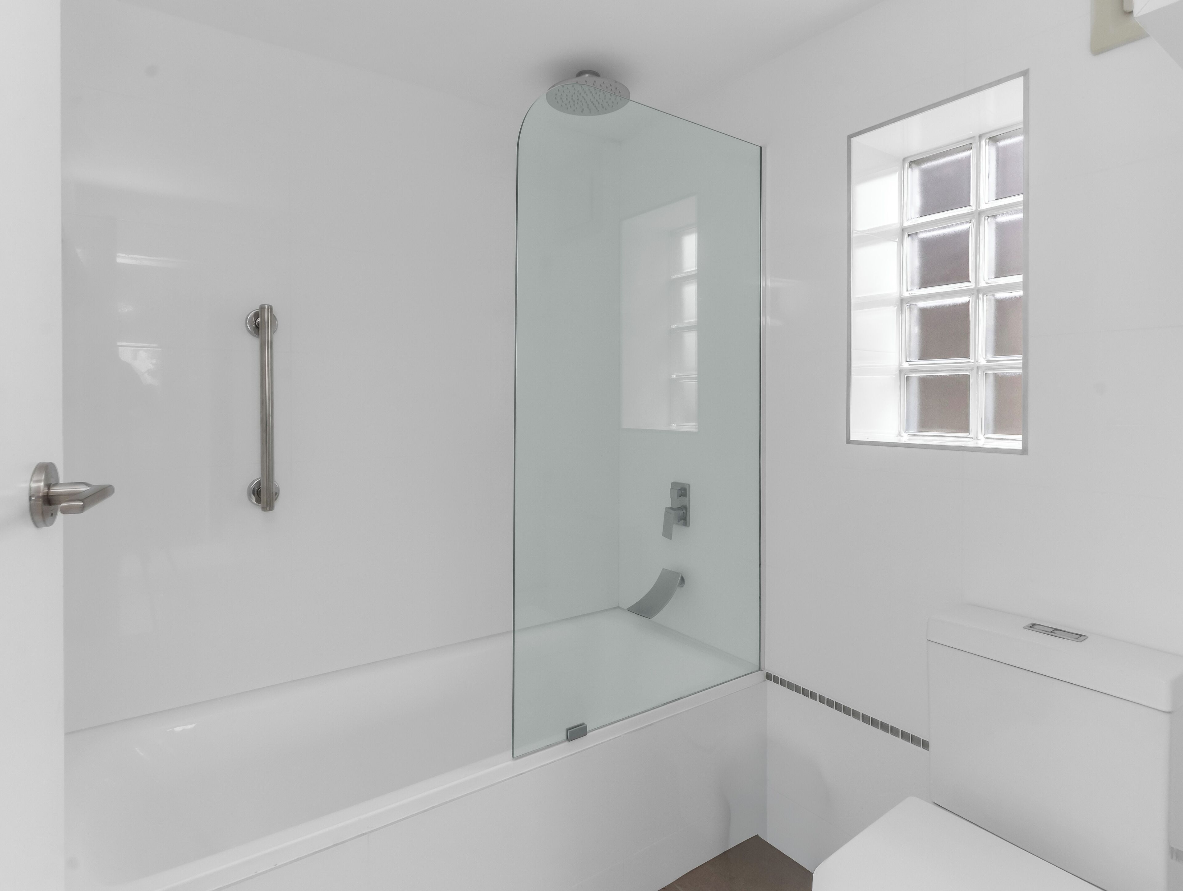 A modern bathroom with a glass-enclosed shower, a white toilet, and a window with frosted glass.