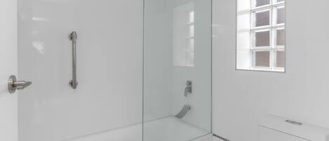 A modern bathroom with a glass-enclosed shower, a white toilet, and a window with frosted glass.