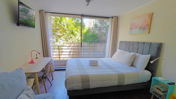A bedroom with a bed, a desk, a chair, a sofa, a nightstand, and a window with a view of greenery. - Un bombón en Santiago Centro (Santiago)