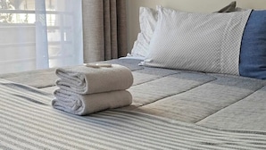 Un lit bien fait, avec une couvre-lit à rayures, une serviette pliée et un oreiller orné d’un motif géométrique.