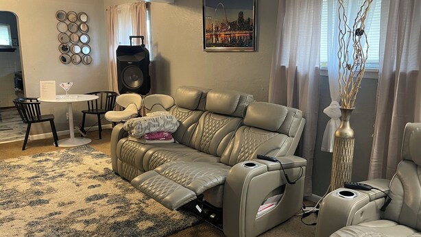 A living room with a beige leather sofa, a small white table, black chairs, a large speaker, and a cityscape painting on the wall. - Delightful 2-bedroom house with AC in Berkeley Iconixx Getaway STL (Berkeley)