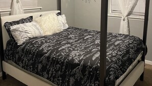 A four-poster bed with a black and white floral bedspread, white pillows, and a decorative wall piece above it. - Delightful 2-bedroom house with AC in Berkeley Iconixx Getaway STL (Berkeley)