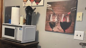 A kitchen with a microwave on a cabinet, a trash can, and two wall art pieces depicting wine glasses. - Delightful 2-bedroom house with AC in Berkeley Iconixx Getaway STL (Berkeley)