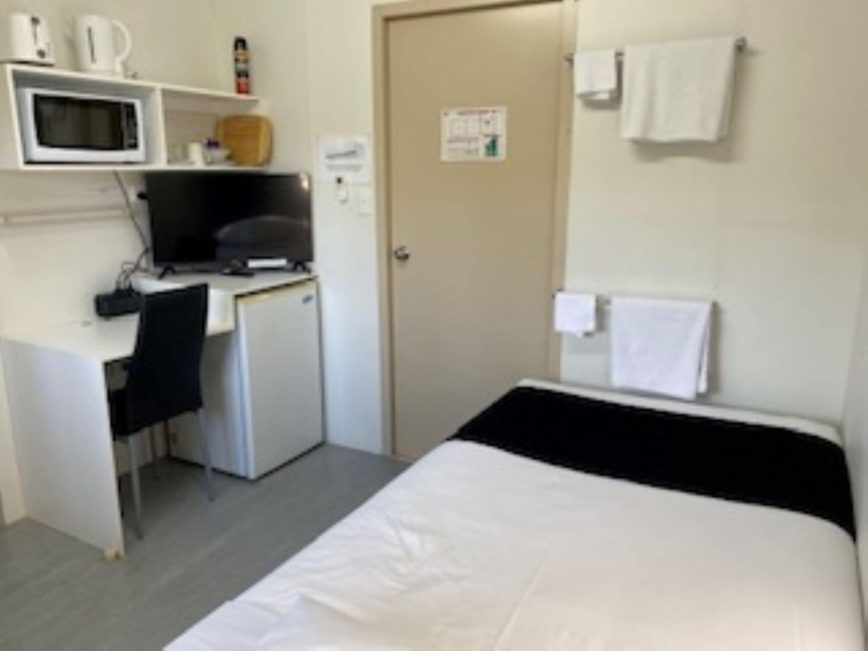 Una camera d'albergo compatta con un letto, una scrivania con un computer, un forno a microonde e un piccolo frigorifero.