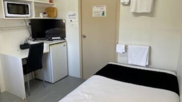 Una camera d'albergo compatta con un letto, una scrivania con un computer, un forno a microonde e un piccolo frigorifero.