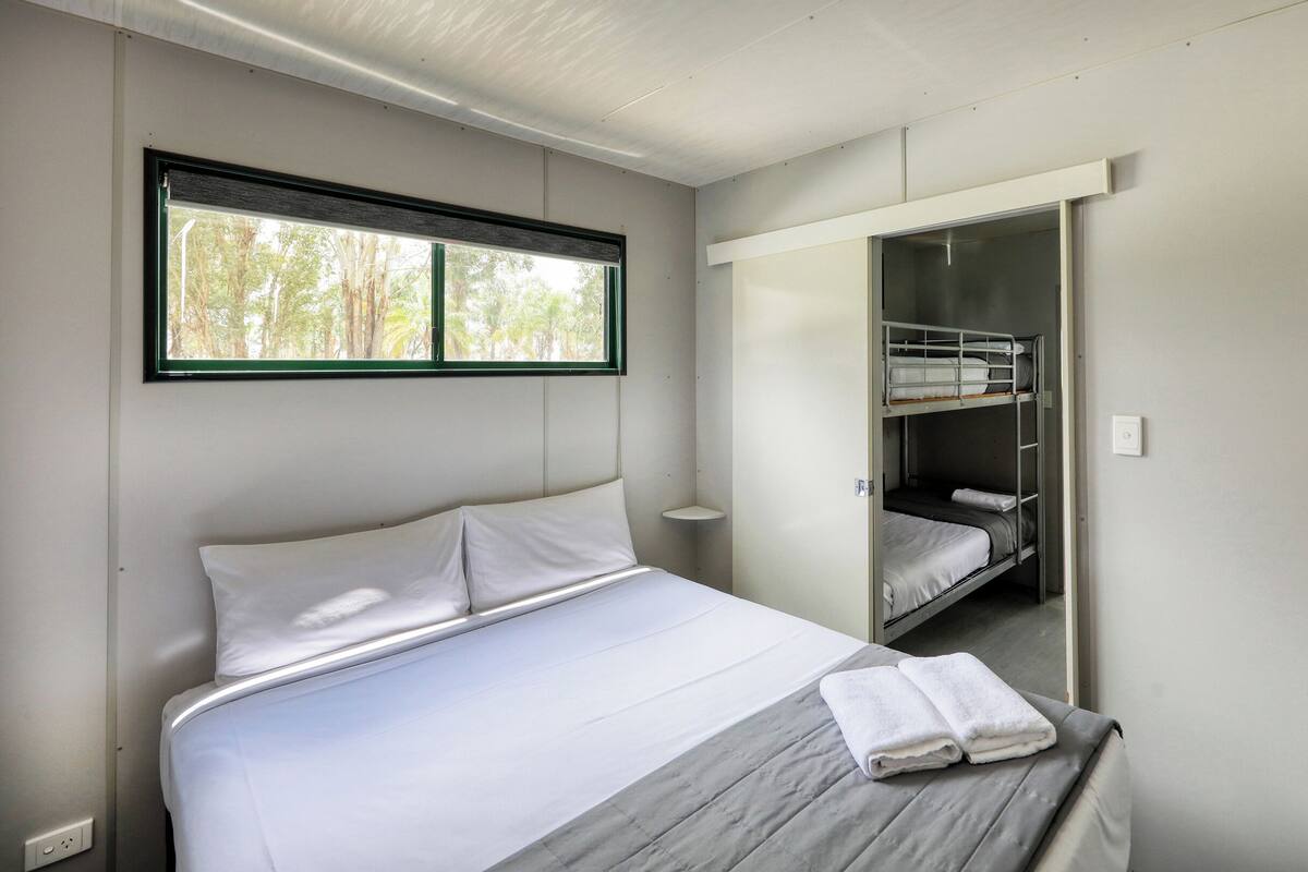 Une chambre à coucher avec un lit, une fenêtre, une armoire et un miroir dans lequel se reflète un lit superposé.