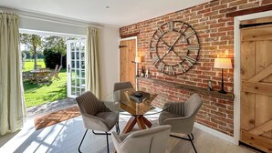 Un comedor con mesa de vidrio, cuatro sillas, un reloj grande y una pared de ladrillo.