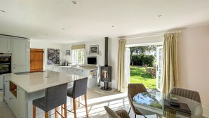 Una cocina moderna con una isla central, un comedor con mesa de vidrio y vistas a un jardín.