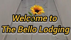 A hallway with a closed door marked with a 'B' and a sunflower graphic with text welcoming to The Bello Lodging.