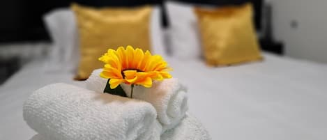 A neatly made bed with a single yellow flower and rolled towels in a hotel room.