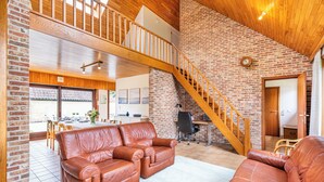Uma sala de estar ampla com teto alto, escada de madeira e área de jantar com vista.