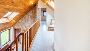 Um quarto espaçoso no estilo loft, com teto inclinado, claraboias, escada de madeira e vista para o exterior.