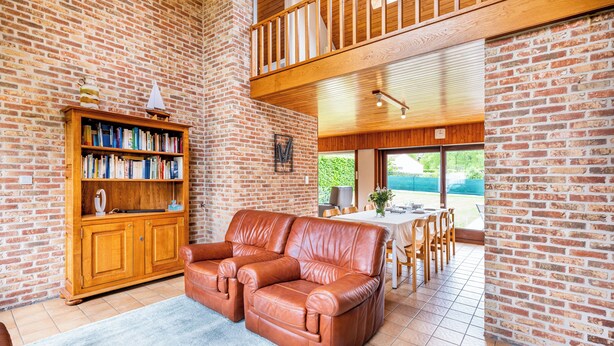 Uma sala de estar ampla com um sofá de couro, uma estante de madeira e um espaço de jantar com mesa e cadeiras.