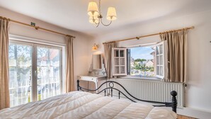 Une chambre à coucher avec un grand lit, une commode, un miroir, une fenêtre avec des rideaux et un radiateur.