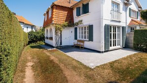 Une maison à deux étages, avec une façade blanche, des volets verts et un toit recouvert de tuiles.