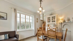 A dining area with a wooden table and chairs, a chandelier, and a white fireplace. - Charming villa located by the dunes (Koksijde)