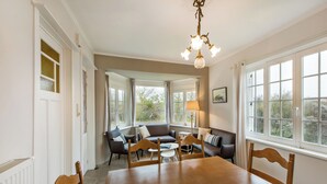 A dining area with a wooden table and chairs, a sofa, and a chandelier. - Charming villa located by the dunes (Koksijde)