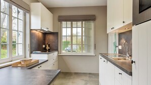 A modern kitchen with white cabinets, a dark countertop, and a window with a view of the outdoors. - Charming villa located by the dunes (Koksijde)