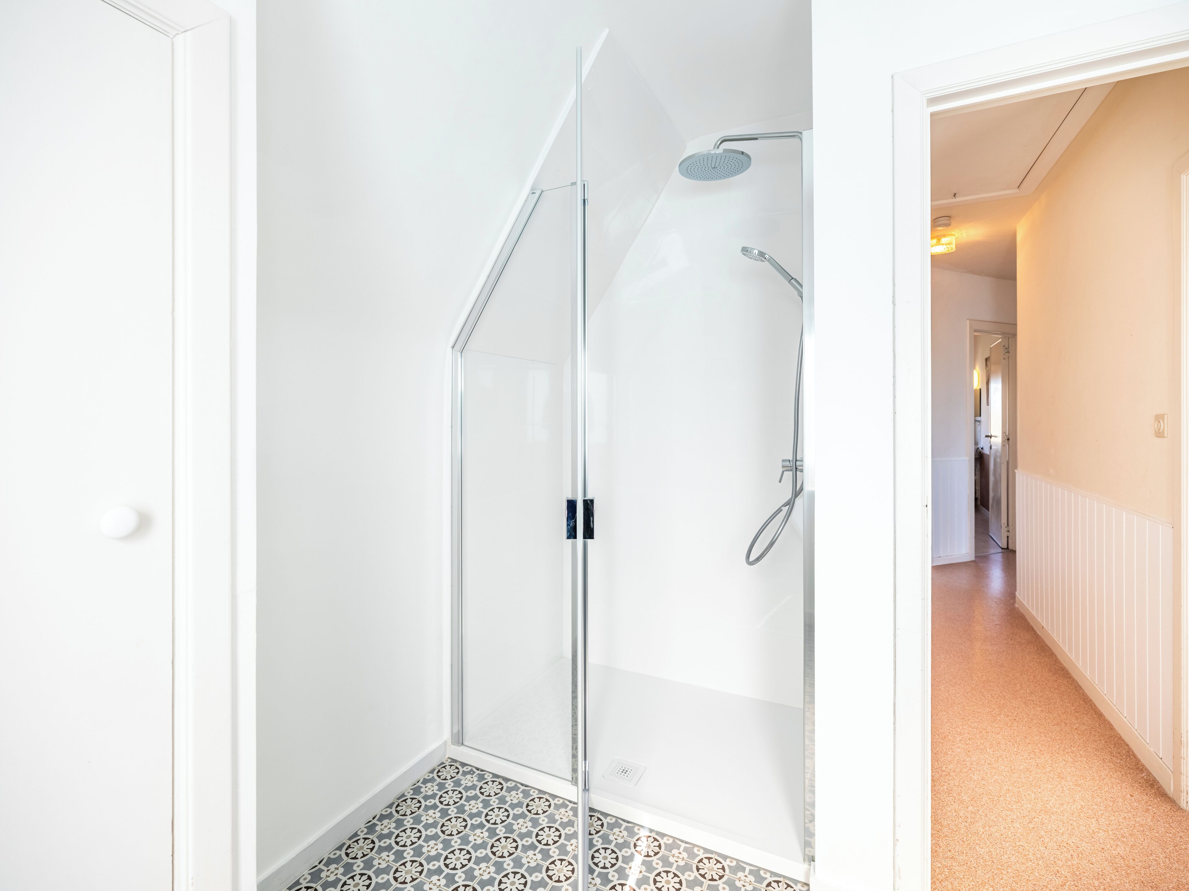 Une salle de bain moderne dotée d’une douche à parois de verre, d’un pommeau de douche à main et d’un robinet mural.