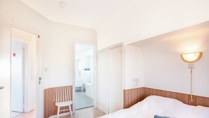 A hotel room with a bed, a chair, a bedside table, and a wall-mounted light fixture. - Authentic coastal villa with quiet location (Koksijde)