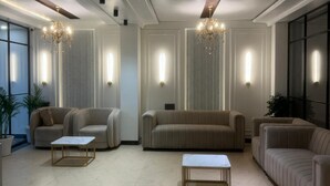 Ein geräumiges Wohnzimmer mit hoher Decke, eingelassener Beleuchtung und einem Kronleuchter. Es gibt drei Sofas und zwei Couchtische.