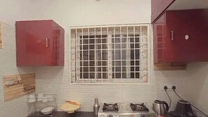 Een kleine keuken met een gasfornuis, een raam met tralies en rode kastjes.