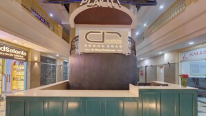 A hotel reception area with a central pillar, a sign for 'CP Suites Sohna Road by Ahuja Residences', and a 'dSalonia' salon to the left. - AR Suites Sohna Road (Gurugram)