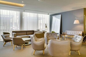 Un hall d’hôtel moderne avec un canapé modulable, des tables rondes et des sièges confortables.