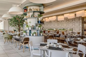 Un restaurante moderno con mesas redondas, sillas y una estructura decorativa central con plantas.