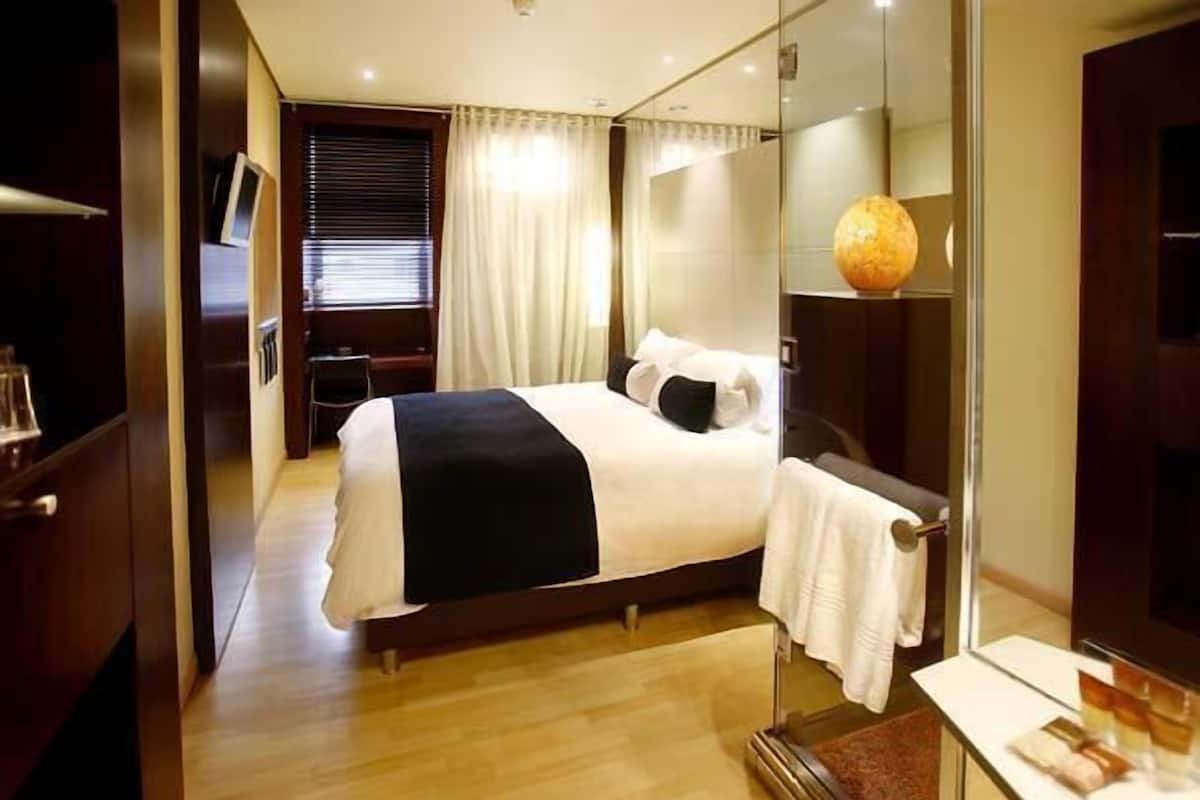 A hotel room with a bed, a bedside table, a mirror, and a window with curtains.