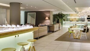 Un hall d’hôtel moderne comprenant un comptoir d’accueil, un espace salon et une grande table à manger.