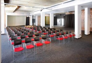 A conference room with rows of chairs, a stage, and a brick wall. - Protea Hotel Fire & Ice! Cape Town (Cape Town)