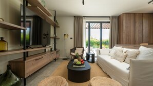 A modern living room with a sofa, coffee table, and wicker ottomans. There is a television on a wooden stand, a floor lamp, and a window with curtains.