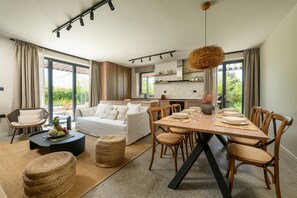 Un salon moderne avec un coin repas, de grandes fenêtres et une cuisine à l’arrière-plan.