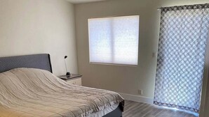 Ein Schlafzimmer mit einem Bett, einem Deckenventilator, einem Fenster mit Jalousien und einem gemusterten Vorhang.