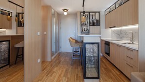 A modern kitchen with wooden cabinets, a glass-fronted wine cooler, and a bar area with stools. - Apartment Skopje Diamond  View (Skopje)